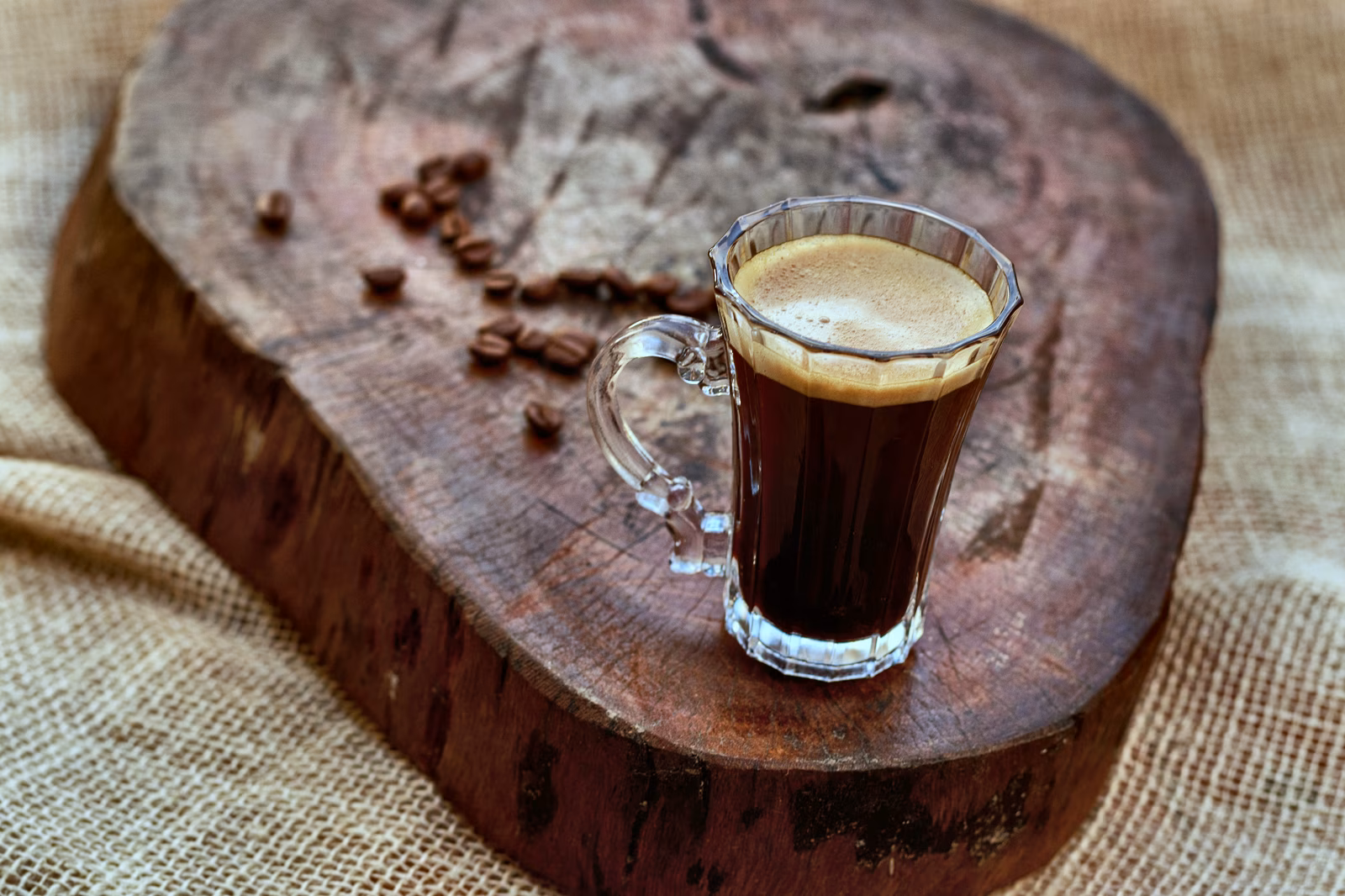 Black coffee in a glass beside coffee beans.