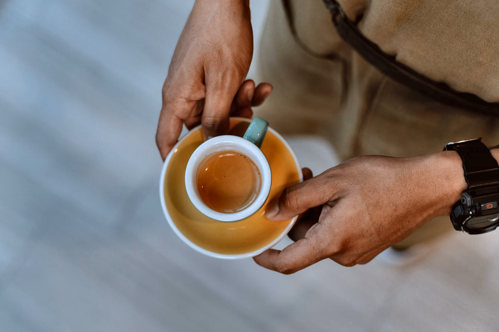 A small espresso cup on a saucer held between two hands.