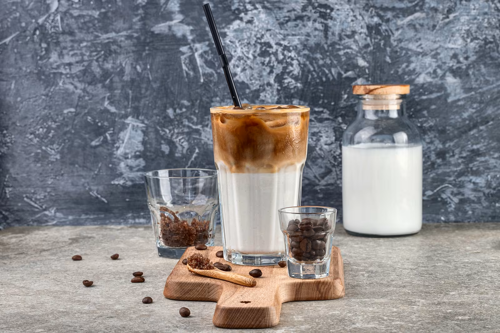 Iced coffee with milk beside a glass of milk and coffee beans.