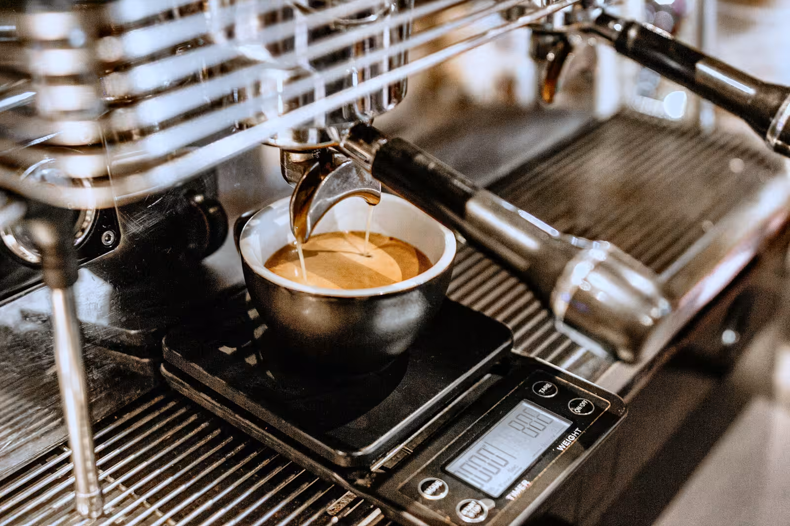 An espresso cup on a scale under an espresso machine.